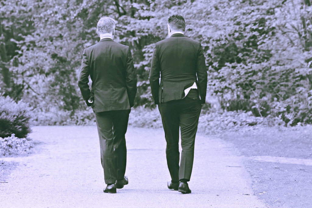 Zwei Männer im Anzug, die spazieren gehen und miteinander reden (Rückenansicht)